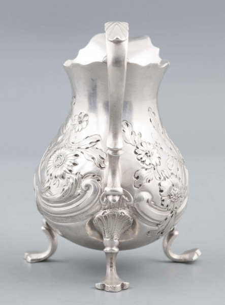 S/Mt/581/ML - Korpus o kształcie gruszkowatym, z wydłużonym wylewem, na trzech nóżkach, ucho profilowane. Krawędź wylewu wycięta faliście, korpus repusowany: na froncie rocaillowy kartusz, po bokach ornamenty wolutowe i kwiatowe.
Na spodzie znaki:
- urząd probierczy w Londynie
- próba Sterling
- oznaczenie roku 