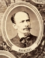 Fotografie w odcieniu sepii umieszczone na tle drzew i roślin, w centralnym miejscu postać kobiety ze sztandarem i aniołkami, wkomponowane widoki budowanej stacji, mostu kolejowego i lokomotywy. Największe zdjęcie w górnej, środkowej części bez podpisu, prawdopodobnie inż. głównej kolei nadwiślańskiej Tadeusz Chrzanowski lub jego następca Walery Titkow. Wśród podobizn pracownicy Biura Głównego Inżyniera: inż. Włodzimierz Stanisławski - pomocnik głównego inżyniera; inż. Feliks Kucharzewski -  pomocnik naczelnika biura; Feliks Kamocki - naczelnik kancelarii; Witold Lanci - naczelnik Wydz. Architektury; dr Wacław Lasocki- służba zdrowia; Władysław Radwan - sprawy zakupu gruntów; inż. Stanisław hr Scipio - projektant mostów kolejowych i jego współpracownicy: inż. Stefan Zieliński, inż. Maurycy Machalski, inż. Feliks Kucharzewski. Fotografia w passe - partout, za szkłem, oprawiona w drewnianą, profilowaną ramę.