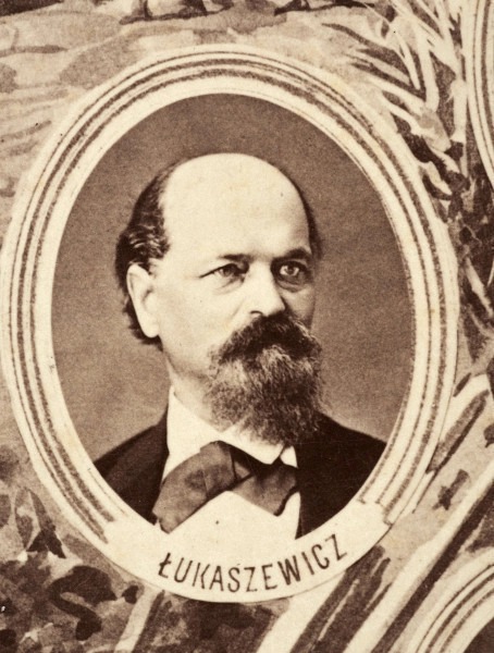 Fotografie w odcieniu sepii umieszczone na tle drzew i roślin, w centralnym miejscu postać kobiety ze sztandarem i aniołkami, wkomponowane widoki budowanej stacji, mostu kolejowego i lokomotywy. Największe zdjęcie w górnej, środkowej części bez podpisu, prawdopodobnie inż. głównej kolei nadwiślańskiej Tadeusz Chrzanowski lub jego następca Walery Titkow. Wśród podobizn pracownicy Biura Głównego Inżyniera: inż. Włodzimierz Stanisławski - pomocnik głównego inżyniera; inż. Feliks Kucharzewski -  pomocnik naczelnika biura; Feliks Kamocki - naczelnik kancelarii; Witold Lanci - naczelnik Wydz. Architektury; dr Wacław Lasocki- służba zdrowia; Władysław Radwan - sprawy zakupu gruntów; inż. Stanisław hr Scipio - projektant mostów kolejowych i jego współpracownicy: inż. Stefan Zieliński, inż. Maurycy Machalski, inż. Feliks Kucharzewski. Fotografia w passe - partout, za szkłem, oprawiona w drewnianą, profilowaną ramę.