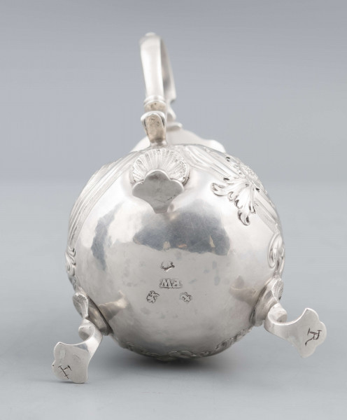 S/Mt/581/ML - Korpus o kształcie gruszkowatym, z wydłużonym wylewem, na trzech nóżkach, ucho profilowane. Krawędź wylewu wycięta faliście, korpus repusowany: na froncie rocaillowy kartusz, po bokach ornamenty wolutowe i kwiatowe.
Na spodzie znaki:
- urząd probierczy w Londynie
- próba Sterling
- oznaczenie roku 