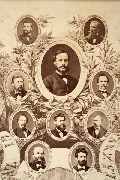 Fotografie w odcieniu sepii umieszczone na tle drzew i roślin, w centralnym miejscu postać kobiety ze sztandarem i aniołkami, wkomponowane widoki budowanej stacji, mostu kolejowego i lokomotywy. Największe zdjęcie w górnej, środkowej części bez podpisu, prawdopodobnie inż. głównej kolei nadwiślańskiej Tadeusz Chrzanowski lub jego następca Walery Titkow. Wśród podobizn pracownicy Biura Głównego Inżyniera: inż. Włodzimierz Stanisławski - pomocnik głównego inżyniera; inż. Feliks Kucharzewski -  pomocnik naczelnika biura; Feliks Kamocki - naczelnik kancelarii; Witold Lanci - naczelnik Wydz. Architektury; dr Wacław Lasocki- służba zdrowia; Władysław Radwan - sprawy zakupu gruntów; inż. Stanisław hr Scipio - projektant mostów kolejowych i jego współpracownicy: inż. Stefan Zieliński, inż. Maurycy Machalski, inż. Feliks Kucharzewski. Fotografia w passe - partout, za szkłem, oprawiona w drewnianą, profilowaną ramę.