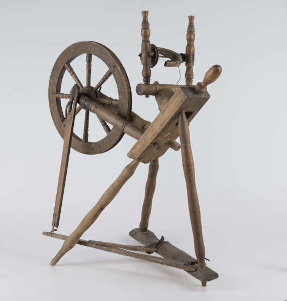 E/16647/ML - Kołowrotek poziomy, drewniany, ozdobnie toczony. Drewno niemalowane. Podstawa to 3 skośnie ustawione nóżki. Dwie z nich osadzone w wąskiej listwie. Górne końce nóżek osadzone w prostokątnej pochyłej grubej desce (11 x 32 x 4 cm). Stanowi ona podstawę do osadzenia koła napędowego i szpuli zwijającej nici. W niej zamocowany uchwyt połączony ze śrubą, która reguluje położenie szpuli. Koło osadzone na metalowej ośce posiada 8 toczonych ozdobnie szprych. Jeden koniec ośki połączony pionową ruchomą listewką z pedałem wprawiającym w ruch kołowrotek. Szpula osadzona również na metalowej ośce.