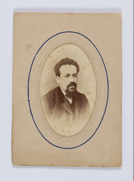 ML/H/F/71 - Fotografia przedstawia dojrzałego mężczyznę zwróconego w prawo. Włosy ciemne, gęste, zaczesane do góry. Wąsy ciemne, dość gęste, łączące się z brodą. Marynarka ciemna z aksamitnym kołnierzem, pod spodem kamizelka i biała koszula. Zdjęcie na firmowym kartoniku zakładu fotograficznego, włożone w passepartout z owalnym wycięciem na fotografię. Na przyklejonym kawałku tekturki w odcieniu szarobłękitnym wypisane czarnym atramentem Henryk Wohl. 