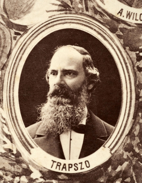 Fotografie w odcieniu sepii umieszczone na tle drzew i roślin, w centralnym miejscu postać kobiety ze sztandarem i aniołkami, wkomponowane widoki budowanej stacji, mostu kolejowego i lokomotywy. Największe zdjęcie w górnej, środkowej części bez podpisu, prawdopodobnie inż. głównej kolei nadwiślańskiej Tadeusz Chrzanowski lub jego następca Walery Titkow. Wśród podobizn pracownicy Biura Głównego Inżyniera: inż. Włodzimierz Stanisławski - pomocnik głównego inżyniera; inż. Feliks Kucharzewski -  pomocnik naczelnika biura; Feliks Kamocki - naczelnik kancelarii; Witold Lanci - naczelnik Wydz. Architektury; dr Wacław Lasocki- służba zdrowia; Władysław Radwan - sprawy zakupu gruntów; inż. Stanisław hr Scipio - projektant mostów kolejowych i jego współpracownicy: inż. Stefan Zieliński, inż. Maurycy Machalski, inż. Feliks Kucharzewski. Fotografia w passe - partout, za szkłem, oprawiona w drewnianą, profilowaną ramę.