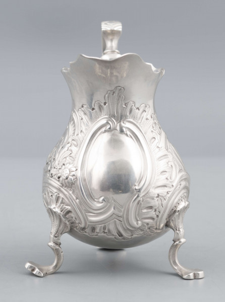 S/Mt/581/ML - Korpus o kształcie gruszkowatym, z wydłużonym wylewem, na trzech nóżkach, ucho profilowane. Krawędź wylewu wycięta faliście, korpus repusowany: na froncie rocaillowy kartusz, po bokach ornamenty wolutowe i kwiatowe.
Na spodzie znaki:
- urząd probierczy w Londynie
- próba Sterling
- oznaczenie roku 