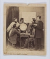 ML/H/F/68 - Jan Bogdanowicz z uczniami na zesłaniu. Fotografia przedstawia sześciu mężczyzn (dwóch siedzących i czterech stojących). Grupa zebrana w pomieszczeniu przy małym kwadratowym stoliku, na którym znajduje się globus, książki, zeszyty i kałamarz z piórem. Jedna z postaci, siedząca po prawej, pisze gęsim piórem. Osoba siedząca naprzeciw wskazuje lewą ręką punkt na globusie. Na ścianie nad stolikiem wisi plansza. Przy niej stoją dwaj mężczyźni - postać po lewej wskazuje coś na planszy prawą dłonią. Nad globusem pochylony jest mężczyzna z brodą w białej długiej koszuli ze stójką (tzw. 