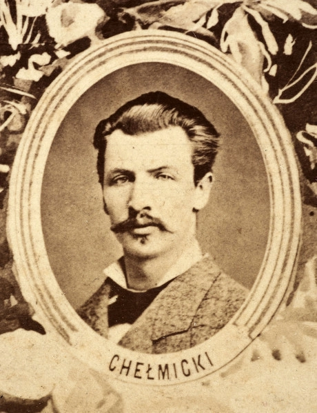 Fotografie w odcieniu sepii umieszczone na tle drzew i roślin, w centralnym miejscu postać kobiety ze sztandarem i aniołkami, wkomponowane widoki budowanej stacji, mostu kolejowego i lokomotywy. Największe zdjęcie w górnej, środkowej części bez podpisu, prawdopodobnie inż. głównej kolei nadwiślańskiej Tadeusz Chrzanowski lub jego następca Walery Titkow. Wśród podobizn pracownicy Biura Głównego Inżyniera: inż. Włodzimierz Stanisławski - pomocnik głównego inżyniera; inż. Feliks Kucharzewski -  pomocnik naczelnika biura; Feliks Kamocki - naczelnik kancelarii; Witold Lanci - naczelnik Wydz. Architektury; dr Wacław Lasocki- służba zdrowia; Władysław Radwan - sprawy zakupu gruntów; inż. Stanisław hr Scipio - projektant mostów kolejowych i jego współpracownicy: inż. Stefan Zieliński, inż. Maurycy Machalski, inż. Feliks Kucharzewski. Fotografia w passe - partout, za szkłem, oprawiona w drewnianą, profilowaną ramę.