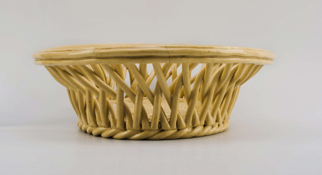 Koszyczek owalny głęboki; dno pełne od zewnątrz obwiedzione warkoczem, boki z okrągłych wałków przeplecionych ukośnie, połączonych profilowaną obręczą tworzącą krawędź. W lustrze (na dnie) dekoracja reliefowa: pośrodku bukiet kwiatów w wazonie, wokół brzegu wić laurowa z owocami. Całość pokryta połyskliwą glazurą w kolorze jasnego ugru.
 