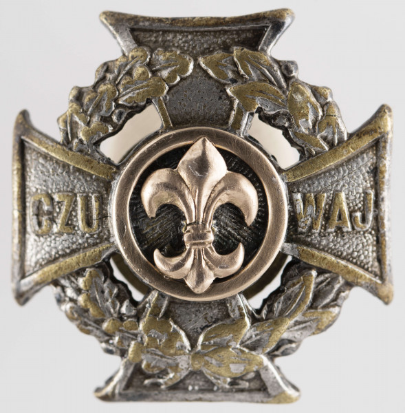 ML/MART/284 - Krzyż harcerski ze złotą lilijką wykonany z metalu, należał do harcerza Stanisława Maciąga. Z tyłu krzyż na zapięcie/nakrętkę. Krzyż harcerski 4-ramienny wykonany z metalu, na środku złota lilijka harcerska w tle liście wawrzynu, na krzyżu napis 