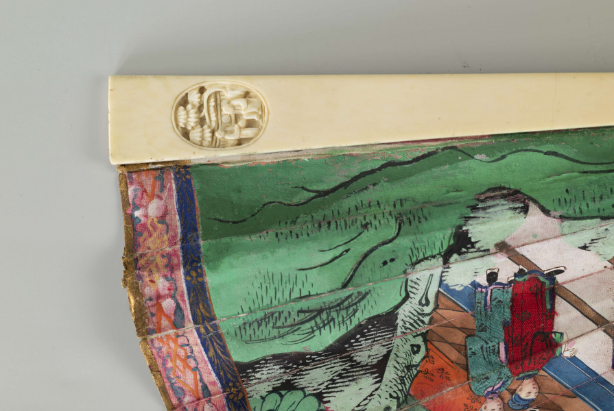 S/R/68/ML - Wachlarz rozkładany. Pokrycie asymetryczne, dwustronne, malowane gwaszem. Twarze postaci wykonane z malowanych, naklejanych, płytek kości słoniowej, ich stroje z malowanych kawałków tkaniny jedwabnej również naklejanych na papier pokrycia. Na wachlarzu przedstawiono sceny rodzajowe w charakterystycznej perspektywie (widziane nieco z góry) w kompozycji kontynuacyjnej, przedstawiają dworzan w towarzystwie wysokiego urzędnika, w scenerii pałacowego ogrodu z pawilonami. Barwne stroje z jedwabiu nawiązują do dworskiej mody i są niezwykle zróżnicowane.   Podkreślone są różnice w formie i detalu stroju. Urzędowe nakrycie głowy, foutou, wyróżnia jedną z przedstawionych postaci, cesarza (?). Stelaż z kości słoniowej, rzeźbiony w motywy roślinne i figuralne, pióra okładzinowe gładkie. Zdobią je pojedyncze, owalne, rzeźbione kompozycje, medaliony ze scenami figuralnymi. Pierścień mosiężny spina stelaż.