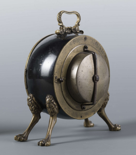 S/Mt/430/ML - Obudowa z brązu w formie bębna leżącego na czterech zwierzęcych łapach, pokrytego czarnym lakierem, z pionowym uchwytem w formie rozciągniętej profilowanej, wolutki. Tarcza zegarowa z mosiądzu, okrągła, moletowana mz malowanymi czarnymi cyframi rzymskimi godzin i oznaczeniem minut; dwie proste wskazówki; osłonieta zamykaną szybką o wypukłym profilu. Zamknięcie z tyłu w postaci okrągłych drzwiczek na zawiasie, z wmontowanym jednym dzwonkiem. Mechanizm mosiężny, o naciągu sprężynowym, z biciem godzin i kwadransów.
Na płycie wewnętrznej mechanizmu grawerowana sygnatura kursywą:
- Jacobus Staigier Lublin
