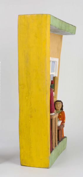 Płaskorzeźba w drewnie lipowym, polichromowana, przedstawiająca wnętrze kuchni, wykonana w jednym kawału drewna. Wnętrze kuchni zaznaczone z lewej strony występem szer. 6,7 cm i gł. 4,5 cm. U góry podkreślony „sufit” wys. 3 cm i gł. 5 cm. Na postumencie wys. 3,5 cm i gł. 4,5 cm. Z lewej strony zakomponowana postać kobiety (z profilu). Kobieta stoi lekko pochylona nad stołem, na którym wałkuje ciasto. Ubrana jest w długą czerwoną suknię w czarne kropki, z długim rękawem.  Na głowie ma zawiązaną, pod brodą, popielatą chustkę, spod której wystają czarne włosy. Twarz płaska, oczy lekko wypukłe, brwi czarne łukowate, nos długi prosty. 
Pod stołem stoi dzbanek, którego brzusiec ozdobiony jest czteropłatkowym kwiatem. Płatki w kolorze czerwony, środek zielony. Wylew podkreślony zielonym paskiem. Z prawej strony przy niskim brązowym stołku, po obu stronach stoją dzieci, które z jednej miski jedzą obiad. Z lewej strony stołka postać chłopca (wys. 12,5 cm) w szarych spodniach, sięgających za kolana i w zielonej koszuli wypuszczonej na spodnie. Twarz chłopca płaska, włosy czarne sięgające do ramion. W prawej ręce chłopiec trzyma łyżkę.  Z prawej – dziewczynka (wys. 13,6 cm), w długiej czerwonej sukience w żółto-czarne ciapki. Włosy czarne, sięgające ramion, twarz płaska. W prawej ręce trzyma łyżkę zanurzoną w misce, lewa opuszczona swobodnie. 
Na wys. 15,5 cm, z prawej strony, okno z kwiatami na parapecie i zasłonkami po bokach, do połowy okna. Wym. okna: wys. 14,5 cm, szer. 11,6 cm.