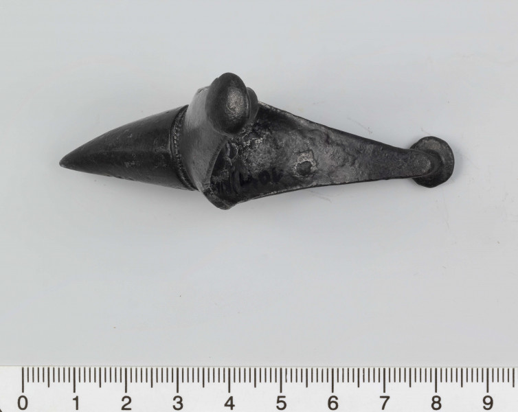 1044/A/ML/1 - Ostroga żelazna z wklęsłym do wewnątrz, łukowatym kabłąkiem. Szeroki przy nasadzie kolca kabłąk zwęża sie stopniowo, przechodząc w wałkowate wygięcia zaczepu, zakończone soczewkowatymi guzkami. Kolec częściowo pusty, ma kształt przegiętego nieznacznie, facetowanego stożka. Przy nasadzie dwie wypiłowane bruzdy z gęsto poprzecznie nacinanym grzbietem powstałym między nimi. Ostroga stanowi element wyposażenia ciałopalnego pochówku złożonego prawdopodobnie w popielnicy. Odkrycia dokonano w 1959 roku przypadkowo w czasie prac rolnych. Oprócz trzech grotów, pochówkowi wojownika towarzyszyły: żelazne umbo, dwie ostrogi, tok brązowy (prawdopodobnie okucie drzewca oszczepu) a także żelazny miecz z miedziana inkrustacją wyobrażającą rzymskich bogów. Pochowany na terenie obecnej wsi Podlodów wojownik należał do elity wojskowej przedstawicieli kultury przeworskiej.
Wymiary dodatkowe: 1,6 cm (podstawa kolca); 1,0 cm (śr. guzków); 3,2 cm (szer. kabłąka przy nasadzie kolca); 0,5 cm (szer. kabłaka przy zaczepach)