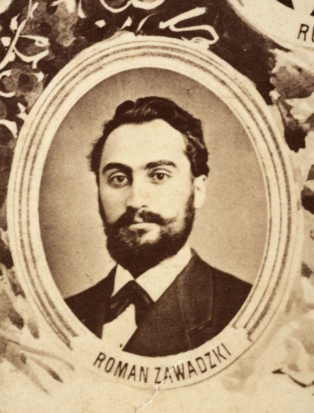 Fotografie w odcieniu sepii umieszczone na tle drzew i roślin, w centralnym miejscu postać kobiety ze sztandarem i aniołkami, wkomponowane widoki budowanej stacji, mostu kolejowego i lokomotywy. Największe zdjęcie w górnej, środkowej części bez podpisu, prawdopodobnie inż. głównej kolei nadwiślańskiej Tadeusz Chrzanowski lub jego następca Walery Titkow. Wśród podobizn pracownicy Biura Głównego Inżyniera: inż. Włodzimierz Stanisławski - pomocnik głównego inżyniera; inż. Feliks Kucharzewski -  pomocnik naczelnika biura; Feliks Kamocki - naczelnik kancelarii; Witold Lanci - naczelnik Wydz. Architektury; dr Wacław Lasocki- służba zdrowia; Władysław Radwan - sprawy zakupu gruntów; inż. Stanisław hr Scipio - projektant mostów kolejowych i jego współpracownicy: inż. Stefan Zieliński, inż. Maurycy Machalski, inż. Feliks Kucharzewski. Fotografia w passe - partout, za szkłem, oprawiona w drewnianą, profilowaną ramę.