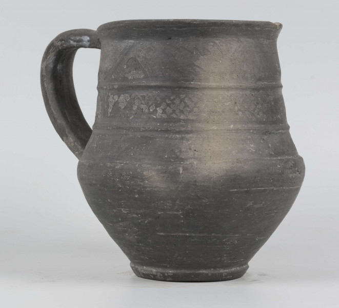 Dno płaskie, wyraźnie wyodrębnione stopką skośnie ściętą ku dołowi; dno wyodrębnione od części przydennej dookolnym wgłębieniem; lekko rozszerzające się ku górze, brzusiec łagodnie zaokraglony, ku górze zwężający się, przechodzący w wysoką, cylindryczną szyjkę; wylew płasko ścięty, rozchylony na zewnątrz; na największej wydętości brzuśca dookolny żłobek; w miejscu przejścia brzuśca w szyję i w połowie szyi dookolny wypukłe listwy; ucho z taśmy środkiem wklęsłej, biegnące od wylewu do załomu brzuśca, szyja zdobiona różnym ornamentem (trzy pasy) przez wygładzenie; powierzchnia gładzona, wyświecona
wymiary dodatkowe: 17,0 cm (obwód); 8,0 cm (śr. dna); 0,3 cm (wys. stopki); 0,5 cm (wys. szyi)