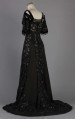 S/T/243/ML - Suknia wizytowa, czarna, uszyta z atłasu jedwabnego, jedwabnego tiulu i aksamitu, haftowana cekinami. Krótki rękaw z jedwabnego czarnego aksamitu, dekolt prostokatny, dość głęboki, wykończony wstawką haftowaną i aksamitem. Kolory są kontrastowe. Spodnia warstwa sukni, z białej tafty i muślinu, widoczna w partiach sukni szytych z czarnego tiulu, dodaje całości elegancji. Brzegi dekoracyjnej wici z tafty zaakcentowane naszytymi cekinami. Suknia do ziemi z tyłu krótki tren. Brak halki. 