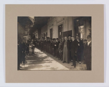 ML/H/F/272 - Przed budynkiem dworca pod dachem od strony peronu stoją, pierwszy od prawej: Leon Przanowski, trzeci - adwokat Edward Rettinger, czwarty - wojewoda Stanisław Moskalewski, szósty - biskup Marian Fulman, siódmy - policjant (komendant wojewódzki?), ósmy - gen. Jan Romer, dowódca DOK Nr II, dalej mężczyźni w melonikach i cylindrach. Fotografia naklejona na tekturę, opisana na odwrociu: 