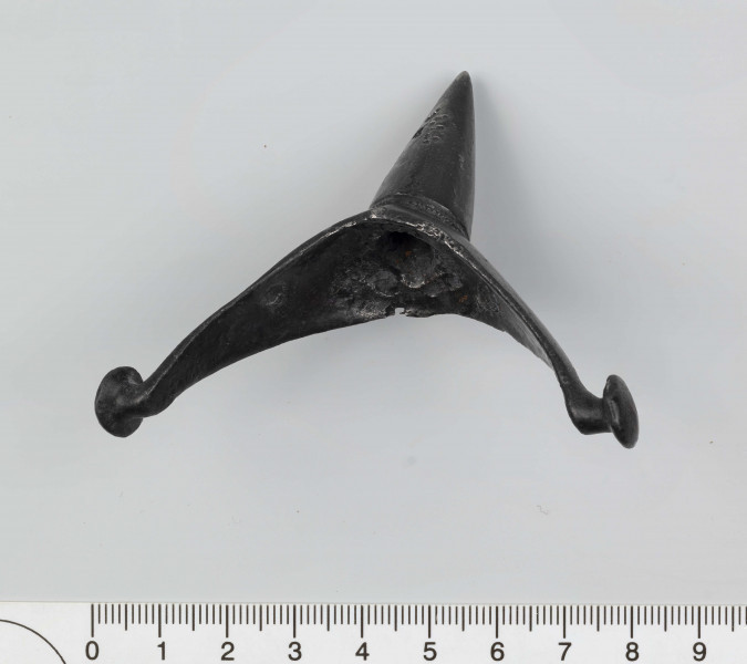 1044/A/ML/1 - Ostroga żelazna z wklęsłym do wewnątrz, łukowatym kabłąkiem. Szeroki przy nasadzie kolca kabłąk zwęża sie stopniowo, przechodząc w wałkowate wygięcia zaczepu, zakończone soczewkowatymi guzkami. Kolec częściowo pusty, ma kształt przegiętego nieznacznie, facetowanego stożka. Przy nasadzie dwie wypiłowane bruzdy z gęsto poprzecznie nacinanym grzbietem powstałym między nimi. Ostroga stanowi element wyposażenia ciałopalnego pochówku złożonego prawdopodobnie w popielnicy. Odkrycia dokonano w 1959 roku przypadkowo w czasie prac rolnych. Oprócz trzech grotów, pochówkowi wojownika towarzyszyły: żelazne umbo, dwie ostrogi, tok brązowy (prawdopodobnie okucie drzewca oszczepu) a także żelazny miecz z miedziana inkrustacją wyobrażającą rzymskich bogów. Pochowany na terenie obecnej wsi Podlodów wojownik należał do elity wojskowej przedstawicieli kultury przeworskiej.
Wymiary dodatkowe: 1,6 cm (podstawa kolca); 1,0 cm (śr. guzków); 3,2 cm (szer. kabłąka przy nasadzie kolca); 0,5 cm (szer. kabłaka przy zaczepach)