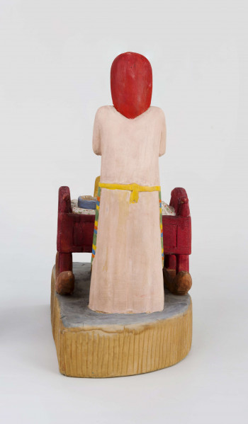 Rzeźba w drewnie lipowym, polichromowana, przedstawiająca postacie matki i dziecka przy kołysce z niemowlęciem. Całość zakomponowana na postumencie wys. 4,4 cm i dł. 22 cm, o kształcie z przodu półokrągłym. Pośrodku usytuowana kołyska na biegunach, wys. 9 cm i dł. 11,2 cm. Kołyska czerwona, ścianki szczytowe ozdobione bukietami składającymi się z trzech wielopłatkowych kwiatów w kolorze żółtym i tulipanowych zielonych liśćmi. W kołysce, w beciku białym, w czerwono-zielone kropki, dziecko, w niebieskiej chustce na głowie. Z lewej strony kołyski postać matki, w długiej jasnoróżowej sukni, w pasie przepasanej fartuchem w żółto-zielono-pomarańczowo-niebieskie poziome pasy. Twarz płaska, nos długi prosty, usta wąskie małe, oczy owalne o podkreślonych białych białkach i czarnych źrenicach, brwi łukowate czarne. Na głowie czerwona chustka zawiązana pod brodą. Spod niej wystają czarne włosy. W rękach trzyma butelkę z mlekiem. Z prawej strony kołyski stoi dziecko w żółtej sukience z niebieskim kołnierzykiem. Twarz dziecka płaska, nos prosty wąski, usta małe, oczy owalne, brwi proste czarne. Włosy czarne, proste sięgające do ramion, zaczesane z grzywką na czole. Ręce wsparte na kołysce. 