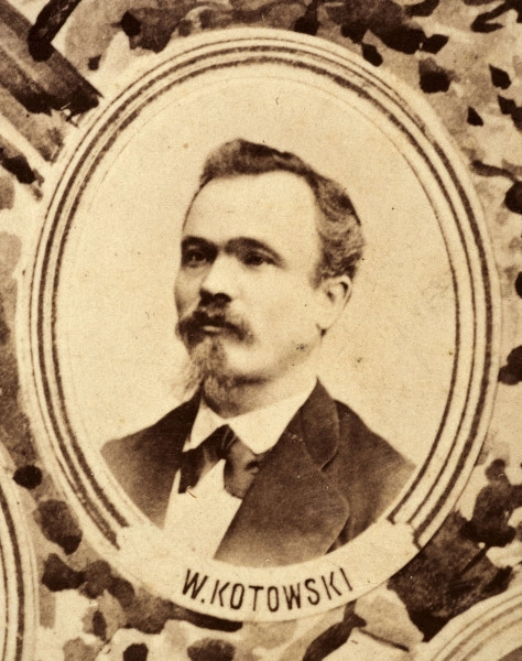 Fotografie w odcieniu sepii umieszczone na tle drzew i roślin, w centralnym miejscu postać kobiety ze sztandarem i aniołkami, wkomponowane widoki budowanej stacji, mostu kolejowego i lokomotywy. Największe zdjęcie w górnej, środkowej części bez podpisu, prawdopodobnie inż. głównej kolei nadwiślańskiej Tadeusz Chrzanowski lub jego następca Walery Titkow. Wśród podobizn pracownicy Biura Głównego Inżyniera: inż. Włodzimierz Stanisławski - pomocnik głównego inżyniera; inż. Feliks Kucharzewski -  pomocnik naczelnika biura; Feliks Kamocki - naczelnik kancelarii; Witold Lanci - naczelnik Wydz. Architektury; dr Wacław Lasocki- służba zdrowia; Władysław Radwan - sprawy zakupu gruntów; inż. Stanisław hr Scipio - projektant mostów kolejowych i jego współpracownicy: inż. Stefan Zieliński, inż. Maurycy Machalski, inż. Feliks Kucharzewski. Fotografia w passe - partout, za szkłem, oprawiona w drewnianą, profilowaną ramę.