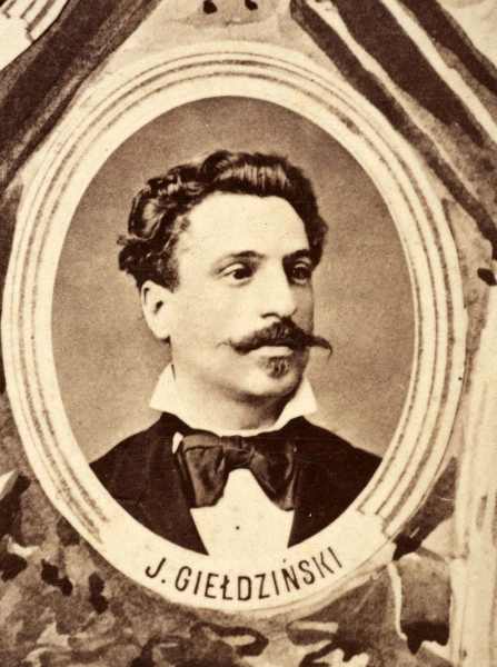 Fotografie w odcieniu sepii umieszczone na tle drzew i roślin, w centralnym miejscu postać kobiety ze sztandarem i aniołkami, wkomponowane widoki budowanej stacji, mostu kolejowego i lokomotywy. Największe zdjęcie w górnej, środkowej części bez podpisu, prawdopodobnie inż. głównej kolei nadwiślańskiej Tadeusz Chrzanowski lub jego następca Walery Titkow. Wśród podobizn pracownicy Biura Głównego Inżyniera: inż. Włodzimierz Stanisławski - pomocnik głównego inżyniera; inż. Feliks Kucharzewski -  pomocnik naczelnika biura; Feliks Kamocki - naczelnik kancelarii; Witold Lanci - naczelnik Wydz. Architektury; dr Wacław Lasocki- służba zdrowia; Władysław Radwan - sprawy zakupu gruntów; inż. Stanisław hr Scipio - projektant mostów kolejowych i jego współpracownicy: inż. Stefan Zieliński, inż. Maurycy Machalski, inż. Feliks Kucharzewski. Fotografia w passe - partout, za szkłem, oprawiona w drewnianą, profilowaną ramę.