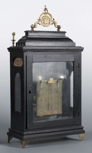 S/Mt/409/ML - Obudowa szafkowa, czworoboczna ze schodkowym zwieńczeniem, pokryta czarną politurą, oszklona z czterech stron, na czterech ażurowych nóżkach z mosiądzu; mosiężny uchwyt, ozdobny, składany a w górnych narożnikach sterczyny w formie płonących wazonów. Mechanizm chodu i bicia o napędzie sprężynowym, z wahadłem i dwoma dzwonkami; bicie godzin i kwadransów, budzik i repetier. Tarcza biało emaliowana z czarnymi cyframi arabskimi godzin i oznaczeniem minut, w niej trzy otwory na osie sprężyn; dwie ozdobne wskazówki. Powyżej tarczy wycięcie z widocznym wahadełkiem kontrolnym i trzy mniejsze emaliowane tarcze: środkowa z sygnaturą: Gottfried / Krohz / Cracovie, boczne z wyłączeniem chodu i bicia.