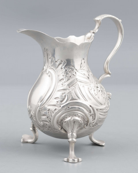 S/Mt/581/ML - Korpus o kształcie gruszkowatym, z wydłużonym wylewem, na trzech nóżkach, ucho profilowane. Krawędź wylewu wycięta faliście, korpus repusowany: na froncie rocaillowy kartusz, po bokach ornamenty wolutowe i kwiatowe.
Na spodzie znaki:
- urząd probierczy w Londynie
- próba Sterling
- oznaczenie roku 