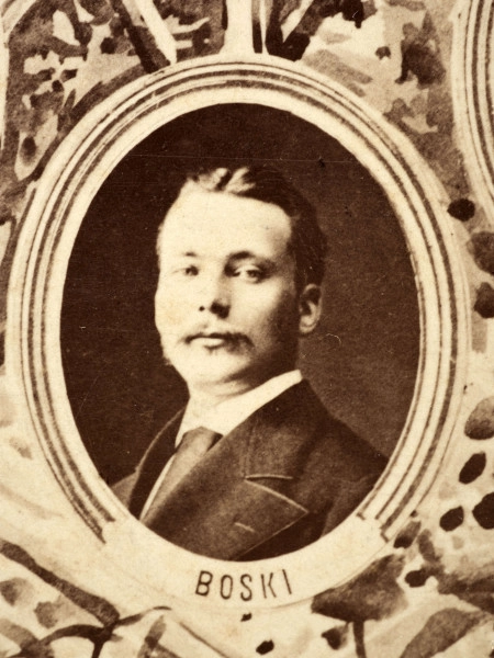 Fotografie w odcieniu sepii umieszczone na tle drzew i roślin, w centralnym miejscu postać kobiety ze sztandarem i aniołkami, wkomponowane widoki budowanej stacji, mostu kolejowego i lokomotywy. Największe zdjęcie w górnej, środkowej części bez podpisu, prawdopodobnie inż. głównej kolei nadwiślańskiej Tadeusz Chrzanowski lub jego następca Walery Titkow. Wśród podobizn pracownicy Biura Głównego Inżyniera: inż. Włodzimierz Stanisławski - pomocnik głównego inżyniera; inż. Feliks Kucharzewski -  pomocnik naczelnika biura; Feliks Kamocki - naczelnik kancelarii; Witold Lanci - naczelnik Wydz. Architektury; dr Wacław Lasocki- służba zdrowia; Władysław Radwan - sprawy zakupu gruntów; inż. Stanisław hr Scipio - projektant mostów kolejowych i jego współpracownicy: inż. Stefan Zieliński, inż. Maurycy Machalski, inż. Feliks Kucharzewski. Fotografia w passe - partout, za szkłem, oprawiona w drewnianą, profilowaną ramę.