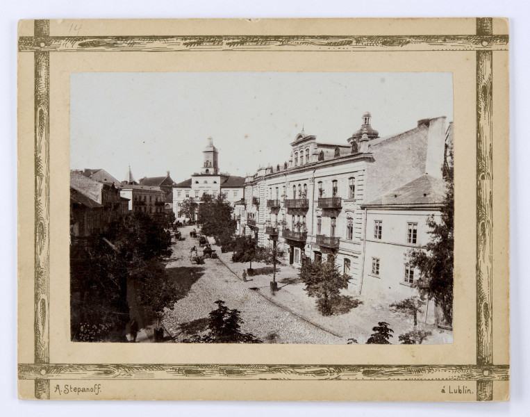 Widok z góry na ulicę Królewską z Nowym Ratuszem w głębi. Po obu stronach łagodnie skręcającej, brukowanej „kocim łbem”, ulicy pierzeje kamienic. Lewa strona w cieniu. Prawa oświetlona. Centralna kamienica z boniowaniem od frontu i balkonami z metalową balustradą. W tle, ponad dachami hełm Bramy Krakowskiej. Chodniki obsadzone drzewami. Widoczne sylwetki przechodniów. Na ulicy wozy i bryczki jadące w kierunku Śródmieścia. W głębi budynek Nowego Ratusza (Magistratu) zamykającego perspektywę ulicy. Front częściowo przysłonięty drzewami. Po lewej wieża Kościoła pw. Św. Ducha.

Fotografia sepiowana, naklejona na tekturę, otoczona ozdobną ramką w kolorze złotym w formie przecinających się na rogach listew. W l. d. rogu nazwisko autora fotografii, w p. d. nazwa miasta. Na rewersie odbitki pieczęci tuszowych Muzeum Nałęczowskiego (okrągła, w kolorze fioletowym) oraz Biblioteki Nałęczowskiej (podłużna, w kolorze fioletowym). U góry odręczny napis informacyjny czarnym tuszem.
