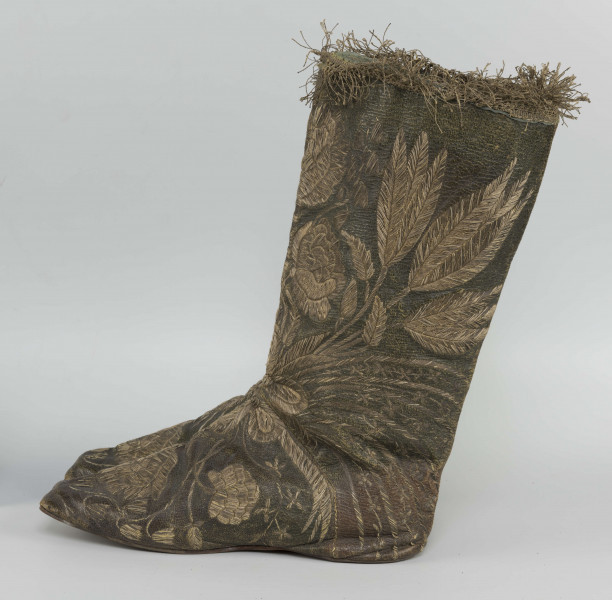 S/T/42/ML - Para butów z wysokimi cholewkami. Cholewka z miękkiej,zielonej skóry,  z dekoracyjnym haftem złotą nicią. Haft z dużym motywem kwiatowym: piwonie, kampanule i drobne kwiatki niezapominajki, tulipany(?), wydłużone liście i wici roślinne, wygięte łukowato.  Wewnatrz buty mają wykończenie białym, cienkim płótnem. Brzegi cholewki obszyte złota koronką z frędzlą. Podeszwy cieńkie z jednego kawałka skóry, bez obcasów, płaskie, z przodu prosto ścięte. Obydwie, skórzane podeszwy mają taki sam wykrój, bez rozróżnienia na lewą i prawą.