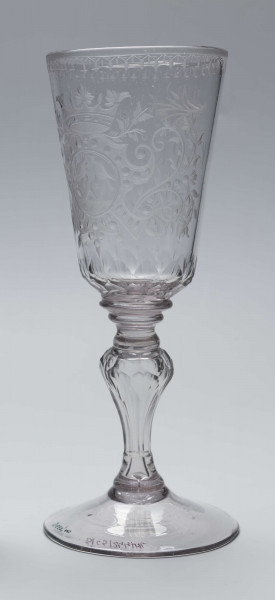 S/CS/244/ML - Stopa okrągła, lekko uniesiona, trzon tralkowy, z pęcherzykiem powietrza, fasetowany, od czaszy oddzielony pierścieniem i dwoma talerzykami, czasza stozkowata, u nasady zaokrąglona, szlifowana w dwa pionowe rzędy owalnych faset. Dekoracja rytowana: na czaszy dwustronna - z jednej strony owalna tarcza z parą gołąbków połączonych dziobkami stojących na serduszkach w rozbudowanym kartuszu z uszakami, z którego wyrastaja gałązki; po drugiej stronie litery 