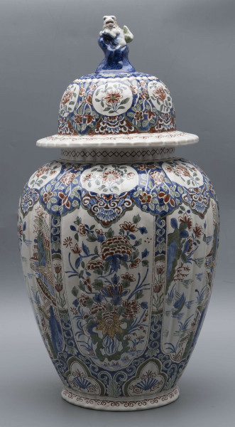 S/CS/546/ML - Wazon owoidalny o niskiej podstawie i niskiej pierścieniowej szyi, powierzchnia drobno kanelowana, pokrywa kopulasta z szerokim kołnierzem, uchwyt w kształcie lwa Fo wspartego prawą łapą na pniu drzewa (?). Dekoracja malowana podszkliwnie w kolorach błękitu, czerwieni, zieleni, żółcieni. W sześciu owalnych, wydłużonych rezerwach na przemian kompozycja kwiatowa z peonią i pejzaż nadrzeczny z architekturą o charakterze orientalnym. U góry - na barkach - sześć owalnych rezerw z kwitnącą gałązką, na dole sześć rezerw trójlistnych z motywem uproszczonej muszli i wolut, na stopie fryz wolutowy, na szyi wąska ukośna kratka. Na pokrywie powtórzona dekoracja z barków, kołnierz biały z fryzem wolutowym analogicznie jak na stopie.
 