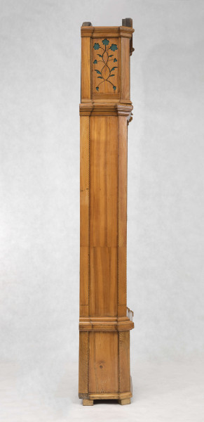 Tarcza w kształcie kwadratu zwieńczonego półkolem, złocona, w narożach ornamenty odlewane z brązu, złocone; pierścień  godzinowy srebrzony z rzymskimi oznaczeniami godzin i zaznaczonymi minutami, wewnątrz tarcza sekundnika, tarczka budzika, plakietka z sygnaturą 