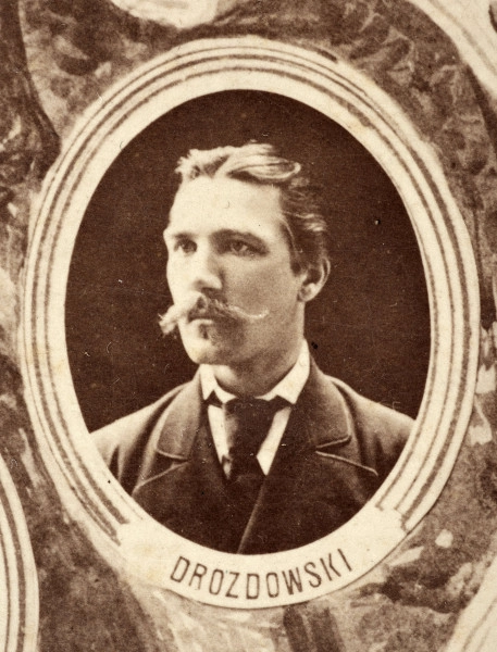 Fotografie w odcieniu sepii umieszczone na tle drzew i roślin, w centralnym miejscu postać kobiety ze sztandarem i aniołkami, wkomponowane widoki budowanej stacji, mostu kolejowego i lokomotywy. Największe zdjęcie w górnej, środkowej części bez podpisu, prawdopodobnie inż. głównej kolei nadwiślańskiej Tadeusz Chrzanowski lub jego następca Walery Titkow. Wśród podobizn pracownicy Biura Głównego Inżyniera: inż. Włodzimierz Stanisławski - pomocnik głównego inżyniera; inż. Feliks Kucharzewski -  pomocnik naczelnika biura; Feliks Kamocki - naczelnik kancelarii; Witold Lanci - naczelnik Wydz. Architektury; dr Wacław Lasocki- służba zdrowia; Władysław Radwan - sprawy zakupu gruntów; inż. Stanisław hr Scipio - projektant mostów kolejowych i jego współpracownicy: inż. Stefan Zieliński, inż. Maurycy Machalski, inż. Feliks Kucharzewski. Fotografia w passe - partout, za szkłem, oprawiona w drewnianą, profilowaną ramę.