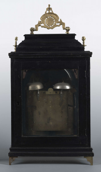 S/Mt/409/ML - Obudowa szafkowa, czworoboczna ze schodkowym zwieńczeniem, pokryta czarną politurą, oszklona z czterech stron, na czterech ażurowych nóżkach z mosiądzu; mosiężny uchwyt, ozdobny, składany a w górnych narożnikach sterczyny w formie płonących wazonów. Mechanizm chodu i bicia o napędzie sprężynowym, z wahadłem i dwoma dzwonkami; bicie godzin i kwadransów, budzik i repetier. Tarcza biało emaliowana z czarnymi cyframi arabskimi godzin i oznaczeniem minut, w niej trzy otwory na osie sprężyn; dwie ozdobne wskazówki. Powyżej tarczy wycięcie z widocznym wahadełkiem kontrolnym i trzy mniejsze emaliowane tarcze: środkowa z sygnaturą: Gottfried / Krohz / Cracovie, boczne z wyłączeniem chodu i bicia.