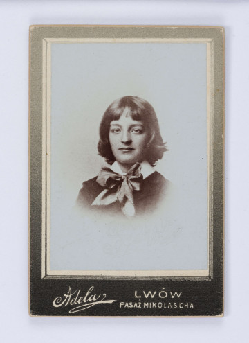 Fotografia przedstawia popiersie młodego Jerzego Pola na jasnym neutralnym tle. Chłopiec ukazany en-face, o jasnych włosach zakrywających uszy. Ubrany w ciemną marynarkę, pod szyją biały kołnierzyk z kokardą. Fotografia naklejona na zielony kartonik.