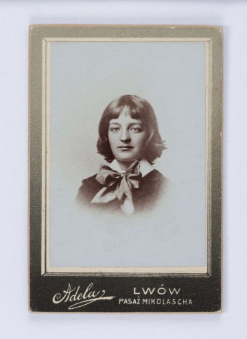 Fotografia przedstawia popiersie młodego Jerzego Pola na jasnym neutralnym tle. Chłopiec ukazany en-face, o jasnych włosach zakrywających uszy. Ubrany w ciemną marynarkę, pod szyją biały kołnierzyk z kokardą. Fotografia naklejona na zielony kartonik.