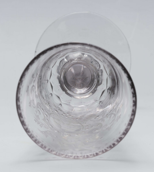 S/CS/244/ML - Stopa okrągła, lekko uniesiona, trzon tralkowy, z pęcherzykiem powietrza, fasetowany, od czaszy oddzielony pierścieniem i dwoma talerzykami, czasza stozkowata, u nasady zaokrąglona, szlifowana w dwa pionowe rzędy owalnych faset. Dekoracja rytowana: na czaszy dwustronna - z jednej strony owalna tarcza z parą gołąbków połączonych dziobkami stojących na serduszkach w rozbudowanym kartuszu z uszakami, z którego wyrastaja gałązki; po drugiej stronie litery 