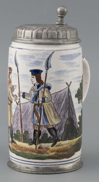 S/CS/64/ML - Korpus cylindryczny z uchem w kształcie litery „C”, pokrywka cynowa, płaska z profilowanym brzegiem i kulistą sterczyną  na zawiasie umocowanym do ucha; profilowana cynowa obręcz otacza dolną krawędź. Pokryty białym szkliwem z wielobarwną dekoracją malowaną skomponowaną przeciwlegle do ucha. Przedstawia ona w uproszczony sposób scenę w obozie  wojskowym: dwaj uzbrojeni kosynierzy stoją na wprost siebie, za nimi widoczny namiot a wokół zielone zarośla i drzewa. Niebo zaznaczone błękitnymi plamami, w tym samym kolorze malowane paski obiegają krawędzie naczynia i zdobią ucho. Tematyka przedstawienia ma wyraźnie patriotyczny charakter nawiązując do powstania kościuszkowskiego.

