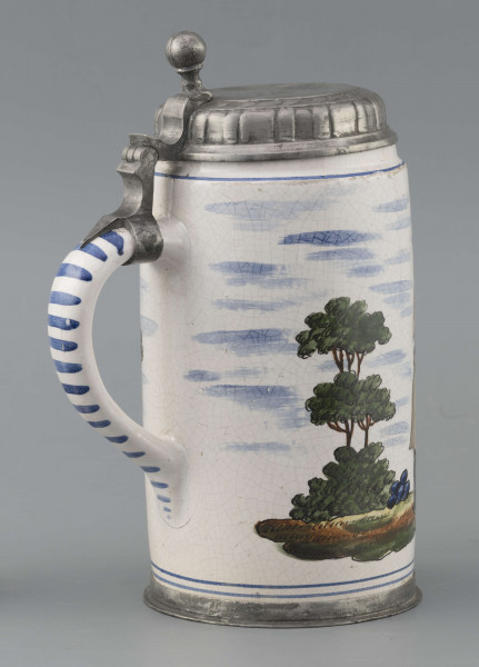 S/CS/64/ML - Korpus cylindryczny z uchem w kształcie litery „C”, pokrywka cynowa, płaska z profilowanym brzegiem i kulistą sterczyną  na zawiasie umocowanym do ucha; profilowana cynowa obręcz otacza dolną krawędź. Pokryty białym szkliwem z wielobarwną dekoracją malowaną skomponowaną przeciwlegle do ucha. Przedstawia ona w uproszczony sposób scenę w obozie  wojskowym: dwaj uzbrojeni kosynierzy stoją na wprost siebie, za nimi widoczny namiot a wokół zielone zarośla i drzewa. Niebo zaznaczone błękitnymi plamami, w tym samym kolorze malowane paski obiegają krawędzie naczynia i zdobią ucho. Tematyka przedstawienia ma wyraźnie patriotyczny charakter nawiązując do powstania kościuszkowskiego.

