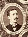 Fotografie w odcieniu sepii umieszczone na tle drzew i roślin, w centralnym miejscu postać kobiety ze sztandarem i aniołkami, wkomponowane widoki budowanej stacji, mostu kolejowego i lokomotywy. Największe zdjęcie w górnej, środkowej części bez podpisu, prawdopodobnie inż. głównej kolei nadwiślańskiej Tadeusz Chrzanowski lub jego następca Walery Titkow. Wśród podobizn pracownicy Biura Głównego Inżyniera: inż. Włodzimierz Stanisławski - pomocnik głównego inżyniera; inż. Feliks Kucharzewski -  pomocnik naczelnika biura; Feliks Kamocki - naczelnik kancelarii; Witold Lanci - naczelnik Wydz. Architektury; dr Wacław Lasocki- służba zdrowia; Władysław Radwan - sprawy zakupu gruntów; inż. Stanisław hr Scipio - projektant mostów kolejowych i jego współpracownicy: inż. Stefan Zieliński, inż. Maurycy Machalski, inż. Feliks Kucharzewski. Fotografia w passe - partout, za szkłem, oprawiona w drewnianą, profilowaną ramę.