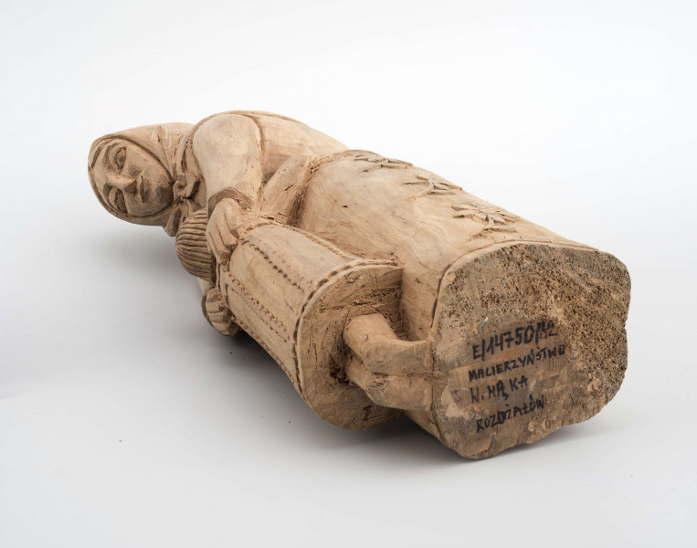 Rzeźba w drewnie lipowym, niepolichromowana, przedstawiająca postać kobiety nachylonej nad dzieckiem, stojącym przy kolanach. Kobieta w chustce na głowie zawiązanej pod brodą, o twarzy trójkątnej, dużych oczach, wąskich ustach. Ubrana w bluzkę z długimi rękawami i serdak z zaznaczoną baskinką , w długiej spódnicy pokrytej stylizowanymi wielopłatkowymi kwiatami na gałązce. U dołu biegnie pasek w formie falistej linii. Kobieta obejmuje rękami dziecko, zwrócone do niej twarzą. Dziecko z włosami sięgającymi do szyi, zaznaczonymi rowkowanymi nacięciami – uczesane z przedziałkiem  pośrodku. W długiej sukience, ozdobionej falistymi liniami poziomymi u dołu i góry, pionowymi pośrodku. 