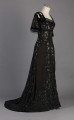 S/T/243/ML - Suknia wizytowa, czarna, uszyta z atłasu jedwabnego, jedwabnego tiulu i aksamitu, haftowana cekinami. Krótki rękaw z jedwabnego czarnego aksamitu, dekolt prostokatny, dość głęboki, wykończony wstawką haftowaną i aksamitem. Kolory są kontrastowe. Spodnia warstwa sukni, z białej tafty i muślinu, widoczna w partiach sukni szytych z czarnego tiulu, dodaje całości elegancji. Brzegi dekoracyjnej wici z tafty zaakcentowane naszytymi cekinami. Suknia do ziemi z tyłu krótki tren. Brak halki. 