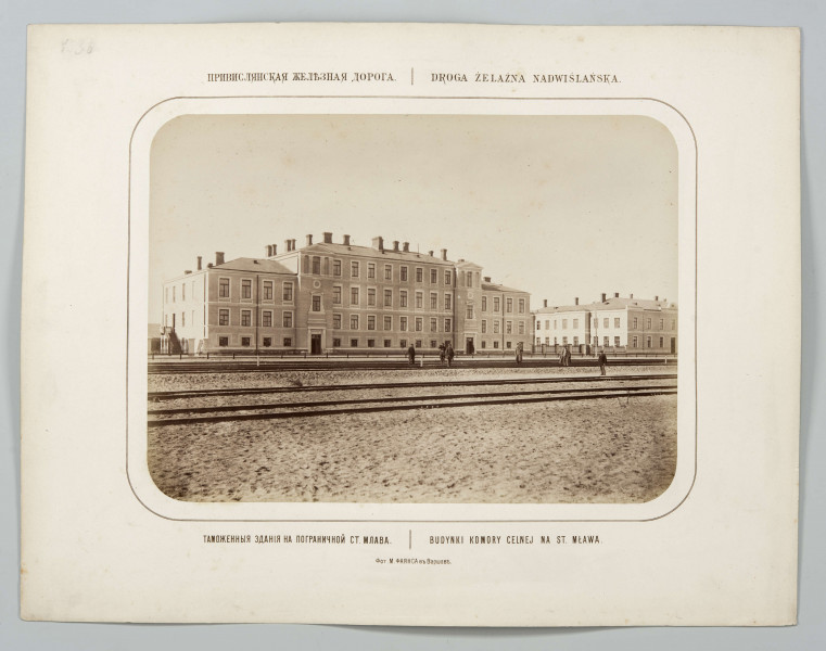 Budynek komory celnej murowany, trzypiętrowy w części środkowej, części boczne dwupiętrowe. Dach kryty blachą, widoczne kominy. Obramienia okien i drzwi jasne. Wejścia usytuowane w dwóch ryzalitach po obu stronach dwupiętrowej części budynku. Przed budynkiem na torach kilkunastu mężczyzn. Na prawo piętrowy budynek.
Fotografia o zaokrąglonych rogach, obrysowana dookoła cienką ramką, naklejona na tekturę. Powyżej i pod fotografią napisy po rosyjsku - z lewej i po polsku- z prawej strony. W dolnej części informacja o autorze zdjęcia po rosyjsku.