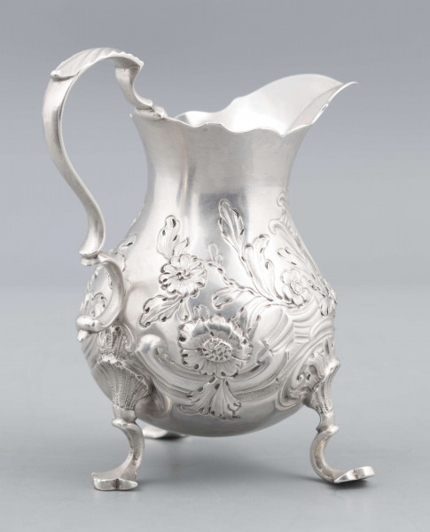 S/Mt/581/ML - Korpus o kształcie gruszkowatym, z wydłużonym wylewem, na trzech nóżkach, ucho profilowane. Krawędź wylewu wycięta faliście, korpus repusowany: na froncie rocaillowy kartusz, po bokach ornamenty wolutowe i kwiatowe.
Na spodzie znaki:
- urząd probierczy w Londynie
- próba Sterling
- oznaczenie roku 