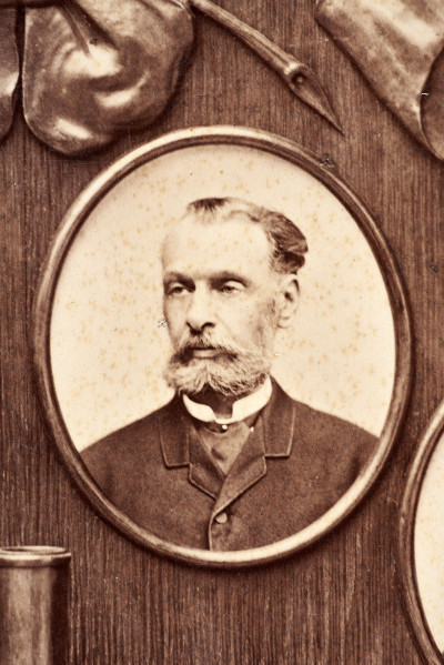 Pośrodku prostokątnego pola o zaokrąglonych narożnikach większa fotografia przyozdobiona wstęgą i gałązkami wawrzynu. Dookoła szesnaście symetrycznie rozmieszczonych mniejszych fotografii. W prawym górnym rogu dr Wacław Lasocki, naczelny lekarz kolei nadwiślańskiej w latach 1875 - 78. W polu ramy w górnej części medalion z płaskorzeźbionym popiersiem z profilu. Przedstawia Leopolda Kronenberga - ojca. Po bokach dwia półleżące aniołki trzymają wieniec laurowy. Po lewej stronie ramy postać robotnika Poleszuka, po prawej pracownika warsztatów kolejowych. W dolnej części front lokomotywy i złoty żeton uprawniający do bezpłatnej jazdy pociągiem I klasy. Fotografia naklejona na tekturę, w dolnej części u dołu sucha pieczęć zakładu fotograficznego.