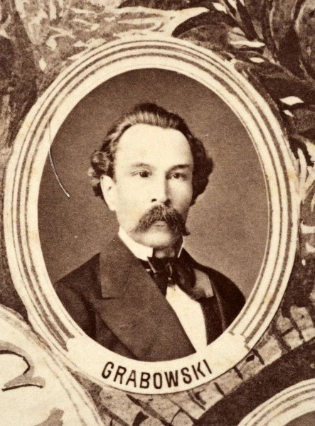 Fotografie w odcieniu sepii umieszczone na tle drzew i roślin, w centralnym miejscu postać kobiety ze sztandarem i aniołkami, wkomponowane widoki budowanej stacji, mostu kolejowego i lokomotywy. Największe zdjęcie w górnej, środkowej części bez podpisu, prawdopodobnie inż. głównej kolei nadwiślańskiej Tadeusz Chrzanowski lub jego następca Walery Titkow. Wśród podobizn pracownicy Biura Głównego Inżyniera: inż. Włodzimierz Stanisławski - pomocnik głównego inżyniera; inż. Feliks Kucharzewski -  pomocnik naczelnika biura; Feliks Kamocki - naczelnik kancelarii; Witold Lanci - naczelnik Wydz. Architektury; dr Wacław Lasocki- służba zdrowia; Władysław Radwan - sprawy zakupu gruntów; inż. Stanisław hr Scipio - projektant mostów kolejowych i jego współpracownicy: inż. Stefan Zieliński, inż. Maurycy Machalski, inż. Feliks Kucharzewski. Fotografia w passe - partout, za szkłem, oprawiona w drewnianą, profilowaną ramę.