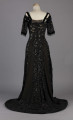 S/T/243/ML - Suknia wizytowa, czarna, uszyta z atłasu jedwabnego, jedwabnego tiulu i aksamitu, haftowana cekinami. Krótki rękaw z jedwabnego czarnego aksamitu, dekolt prostokatny, dość głęboki, wykończony wstawką haftowaną i aksamitem. Kolory są kontrastowe. Spodnia warstwa sukni, z białej tafty i muślinu, widoczna w partiach sukni szytych z czarnego tiulu, dodaje całości elegancji. Brzegi dekoracyjnej wici z tafty zaakcentowane naszytymi cekinami. Suknia do ziemi z tyłu krótki tren. Brak halki. 