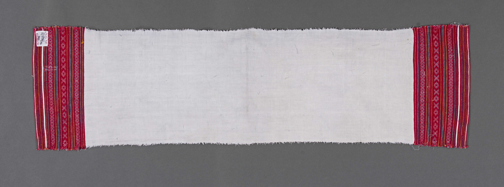 Ręcznik z samodziałowego płótna tkanego splotem prostym. Brzegi dolne, na szer. 14,5 cm, ozdobione ornamentem tkackim zw. pereborami. Ułożony pasowo, złożone z motywów geometrycznych w postaci rombów, kształtów litery X oraz drobnych prążków, w kolorze niebieskim, pomarańczowym i czerwonym.