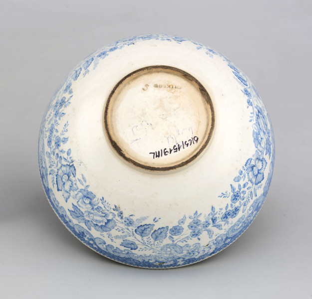 Miseczka półkulista, na niskiej, okrągłej stopce. Zdobiona od strony zewnetrznej i wewnętrznej nadrukiem w kolorze błękitnym z wzorem wolut i ukwieconych gałązek róży i goździków. W lustrze scena w kolorze czarnym przedstawiająca młodą dziewczynę w ogrodzie z elementami 